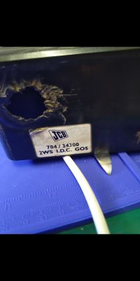 Spalona obudowa z etykietą JCB 704/34300 i widocznym przewodem wychodzącym z dołu.