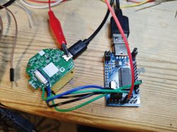 Programming a PCB with a USB Programmer A PCB of an electronic device connected to a USB programmer by several wires, all placed on a wooden surface.