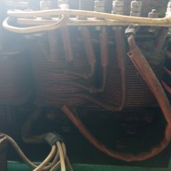 Zbliżenie na uzwojenia i przewody wewnątrz starego agregatu prądotwórczego, z widocznymi podłączeniami kabli i nakrętkami.