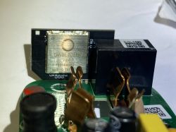 Close-up of a PCB with a relay and a metal module with markings; copper spring contacts visible.