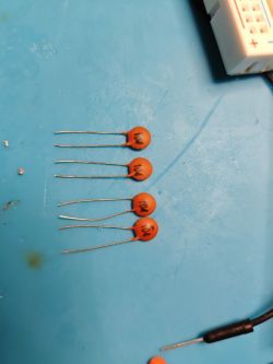 Five orange ceramic capacitors 0.1 µF on a blue electronics work mat.