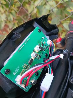 Zdjęcie przedstawia otwarty panel elektryczny hulajnogi z widocznymi przewodami i płytką drukowaną.