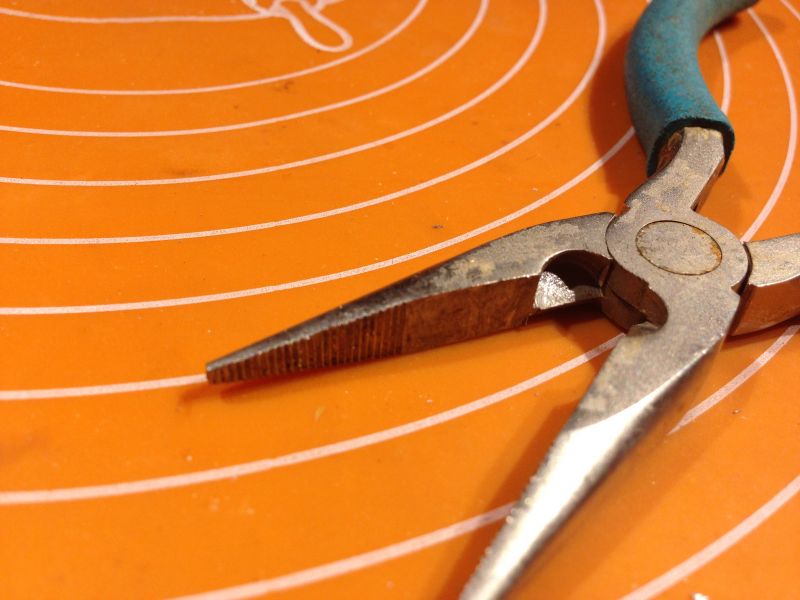 Zbliżenie na zużyte kombinerki na pomarańczowej powierzchni.