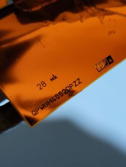 Zbliżenie na płytkę z pomarańczowego materiału z widocznymi oznaczeniami i symbolami.