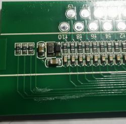 Fragment zielonej płytki drukowanej z elementami elektronicznymi.