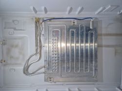 Wnętrze lodówki z odsłoniętą metalową płytą parownika, przewodami i czujnikiem w prawym górnym rogu.