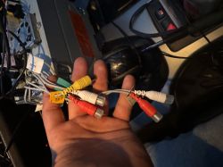 Osoba trzymająca różnokolorowe kable RCA w środku samochodu.