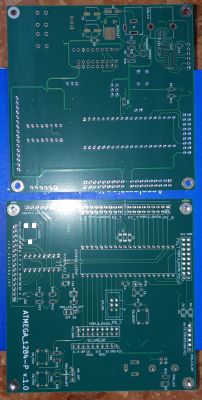 Dwa zielone obwody drukowane, z widocznym oznaczeniem ATMEGA1284P v1.0, leżące na niebieskim tle.