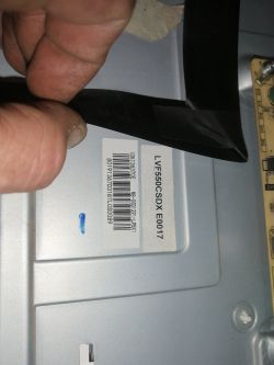 Hand holds black tape by a silver device housing with labels “LVF550CSDX E0017” and a barcode