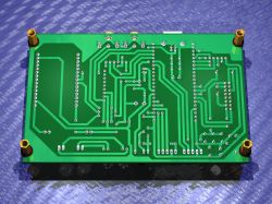 Bottom side of a green PCB with many traces and solder points, plus four standoffs at the corners