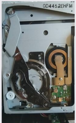 Zdjęcie wnętrza mechanizmu zmieniarki CD z widocznymi elementami metalowymi i elektronicznymi.