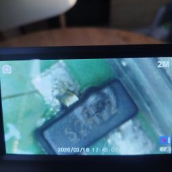 Ekran aparatu pokazujący zbliżenie elementu SMD na zielonej płytce PCB; oznaczenie na elemencie jest nieczytelne.