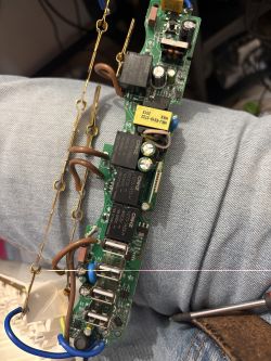 PCB of a DIN-rail switch with relays, transformer, and wires, resting on denim-covered legs