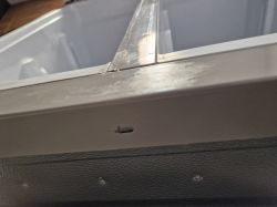 Zbliżenie na element konstrukcyjny w lodówce, z widocznym metalowym i plastikowym fragmentem.