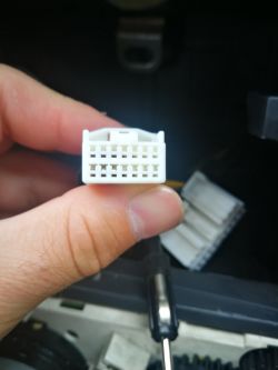 Biała kostka elektryczna trzymana w dłoni na tle części samochodu.