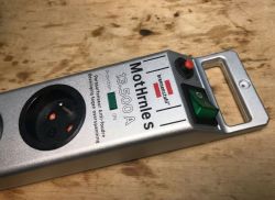 Silver power strip with one socket and green switch on wooden surface