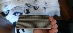Osoba trzymająca matrycę LED 16x16 pikseli w dłoni, na tle pościeli z wzorem.