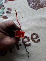 Osoba trzyma czerwoną kostkę elektryczną z wciśniętą fioletową blokadą.