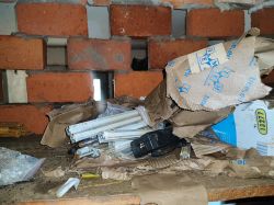 Exposed brick wall with scattered, damaged cables and paper.