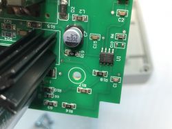 Fragment zielonej płytki drukowanej z elementami elektronicznymi, w tym kondensatorem, chipem i radiatorami.