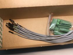 Several gray wires with black ends and a plastic bag with green terminals in a cardboard box.