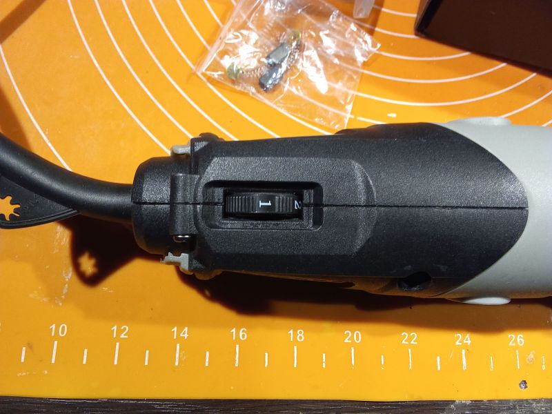 Szczegółowy widok szlifierki z kablem i akcesoriami na pomarańczowej macie mierniczej.