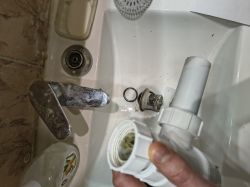 Umywalka z rozebranym odpływem; widoczna metalowa część korka i trzymany biały syfon z tworzywa