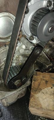 Widok na mechanizm silnikowy z paskiem i kołem zębatym, z widocznym drewnianym podparciem.