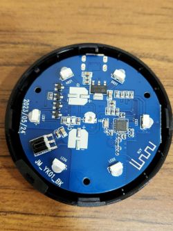 A blue printed circuit board with electronic components mounted in a round casing.