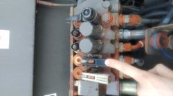 Palec wskazuje czarny suwak na bloku hydrauliki z przewodami i złączami