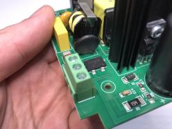 Zbliżenie na fragment płytki drukowanej z podzespołami elektronicznymi, trzymanej w dłoni.