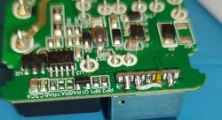 Close-up of a circuit board with electronic components, a soldered wire, and yellow Kapton tape covering part of the board.