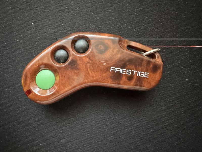 Brązowy pilot typu bumerang „Prestige” z trzema przyciskami i kółkiem na brelok, na czarnym tle