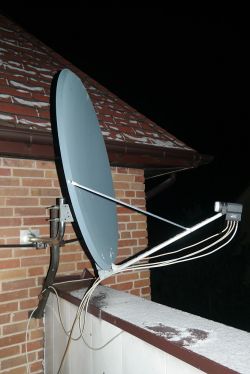 Large satellite dish mounted on a balcony next to a brick house wall in winter