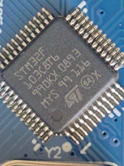 STM32F103C8T6 Microcontroller on PCB Close-up of an STM32F103C8T6 microcontroller on a blue PCB, with visible chip markings and soldered pins.