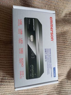 Dekoder Emmerson T145HD w opakowaniu, leżący na dywanie.