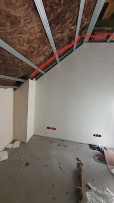Sufit z widoczną izolacją z wełny mineralnej oraz metalowymi belkami konstrukcyjnymi, z zaznaczoną na czerwono przewidywaną trasą przewodu wentylacyjnego.