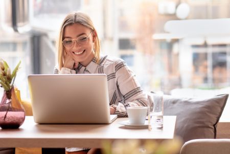 Kobieta pracująca na laptopie w kawiarni Kobieta w okularach pracuje na laptopie przy stoliku w kawiarni