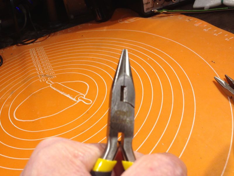 Kombinerki trzymane w dłoni na pomarańczowej macie.