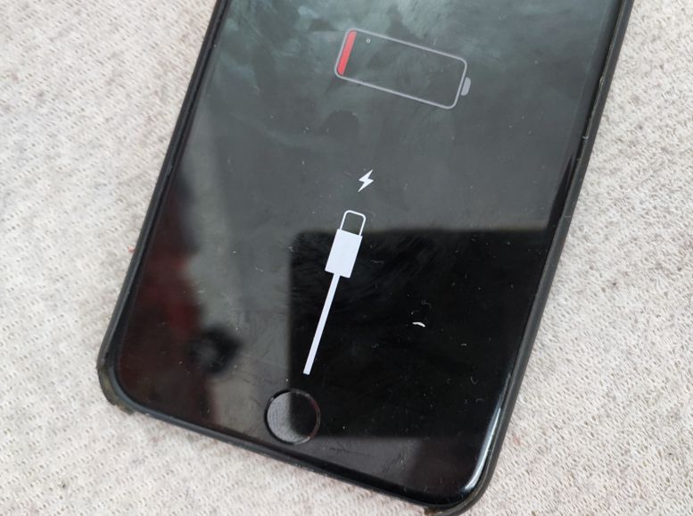 Zbliżenie na ekran telefonu z ikoną rozładowanej baterii i kablem zasilania