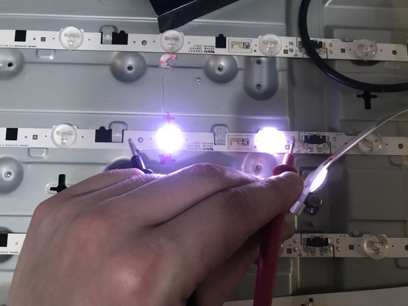 Testing LED Backlight in a TV A hand holding power supply probes tests the LED backlight in a TV.