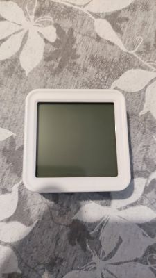 LCD display in a white frame on a gray floral pattern background.