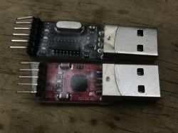 Two USB to TTL adapters with female header pins on a wooden surface
