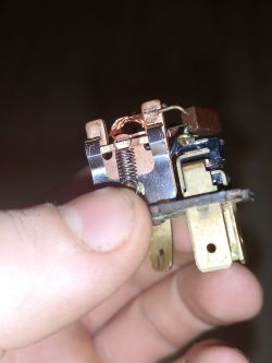 Osoba trzyma przekaźnik elektromagnetyczny z widocznymi terminalami i miedzianą cewką.