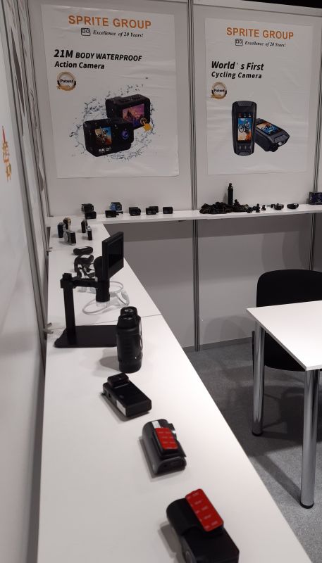 Stoisko firmy na targach elektroniki, wyświetlające różne modele kamer sportowych i rowerowych.