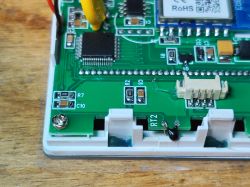 Close-up of a thermostat PCB with an IC, shielded module, and white connector inside a plastic housing