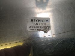 Etykieta na metalowej powierzchni z widocznym przesunięciem i uszkodzeniem.