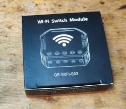 Wi-Fi Switch Module QS-WIFI-S03 Packaging Box of the Wi-Fi Switch Module QS-WIFI-S03 on a wooden background.