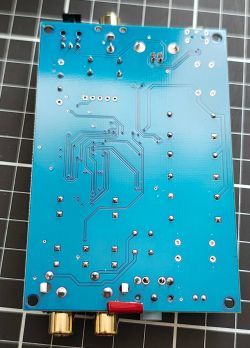 Spód niebieskiej płytki PCB urządzenia audio z widocznymi ścieżkami i lutami, na macie w kratkę