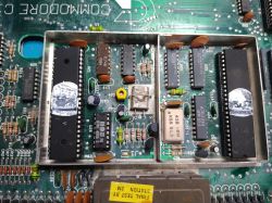 Zbliżenie na wnętrze starego komputera Commodore, ukazujące płytę główną z układami scalonymi i elektronicznymi komponentami.